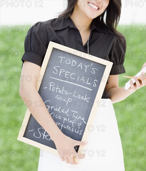 Asian waitress holding chalkboard with day's specials