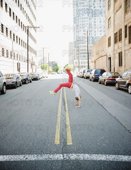 Hispanic teenage boy doing back flip in urban street