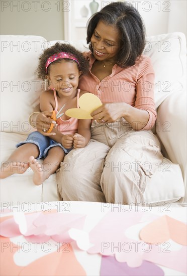 African grandmother cutting out heart-shape with granddaughter