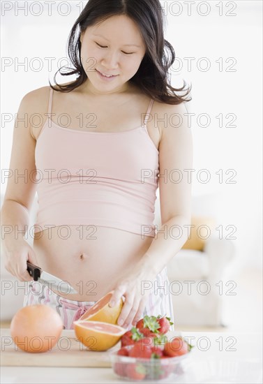 Pregnant Asian woman cutting grapefruit