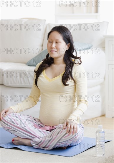 Pregnant Asian woman meditating on yoga mat