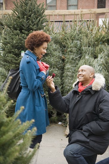 African man giving girlfriend engagement ring in Christmas tree lot