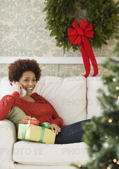 Mixed race woman holding Christmas presents talking on telephone