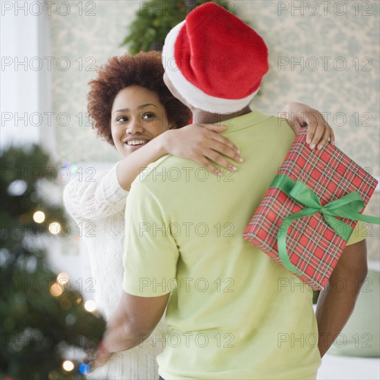 Mixed race woman hugging boyfriend and holding Christmas present