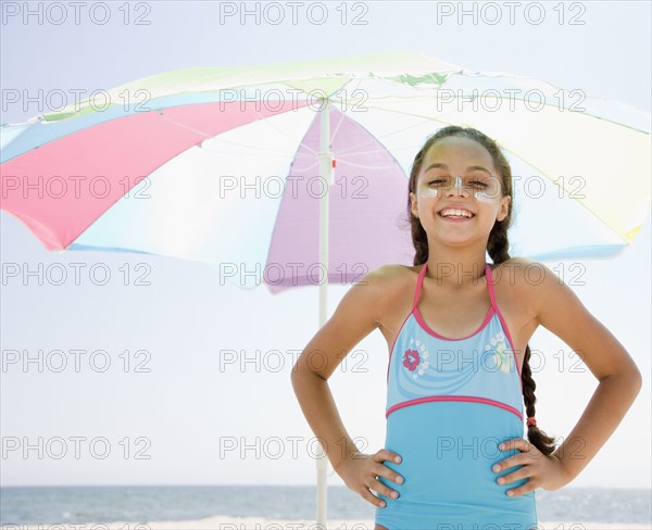 Hispanic girl with sunscreen under umbrella on beach