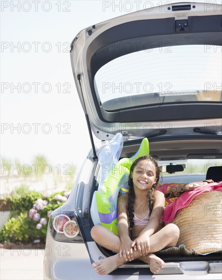 Hispanic girl sitting in hatchback of car