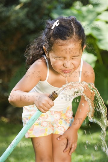 Hispanic girl drinking from hose