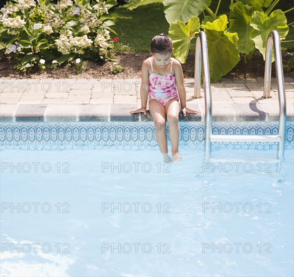 Hispanic girl sitting on edge of swimming pool