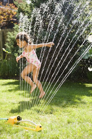 Hispanic girl playing in water sprinkler