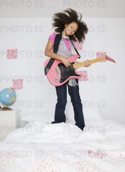 African girl playing guitar on bed