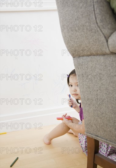 Toddler girl hiding behind chair