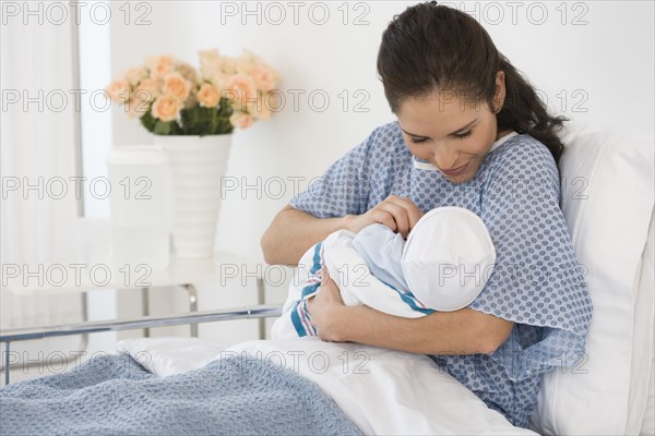 Hispanic mother holding newborn baby in hospital bed