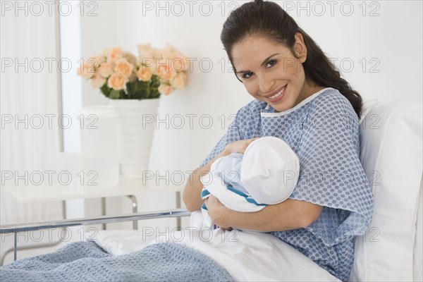 Hispanic mother holding newborn baby in hospital bed