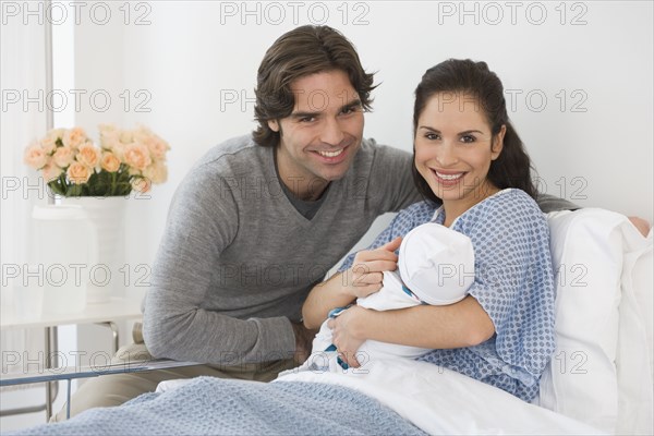 Hispanic couple holding newborn baby in hospital bed