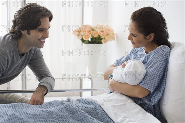 Hispanic couple holding newborn baby in hospital bed