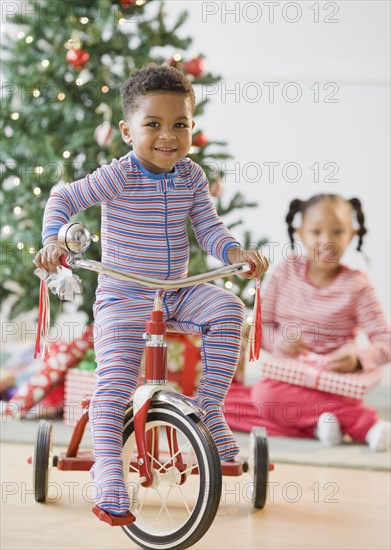 African American boy riding tricycle near Christmas tree