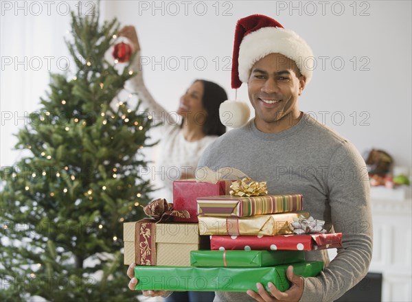 African American man holding Christmas gifts by tree