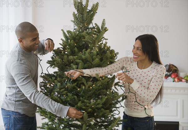 Couple placing string lights on Christmas tree