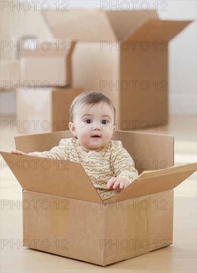 Mixed race baby girl sitting in cardboard box