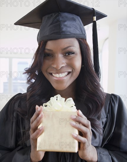 African woman in graduation cap and gown holding gift