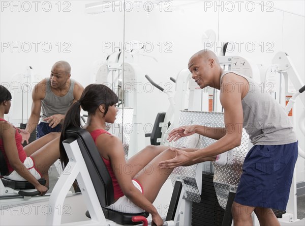 African man helping woman on exercise equipment