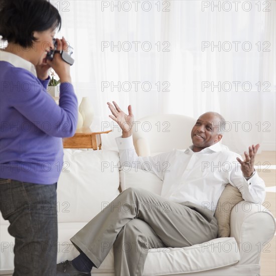 African woman recording husband in livingroom
