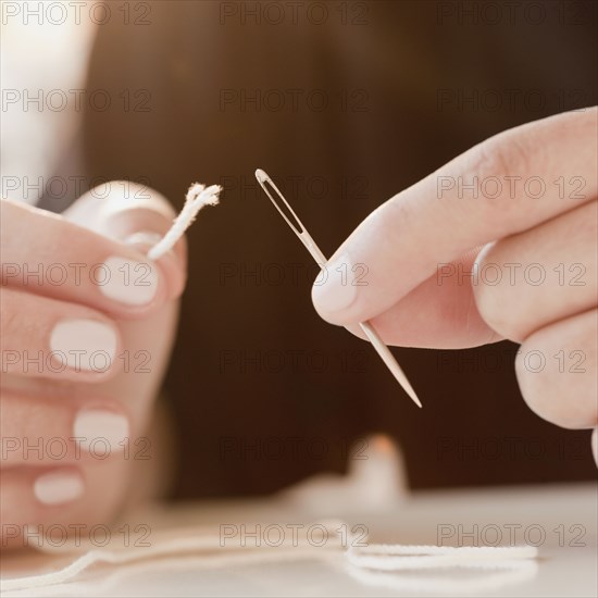 Woman stringing frayed thread through needle