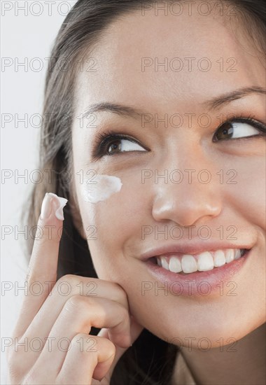 Mixed race woman applying cream under eyes