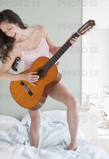 Mixed race woman playing guitar on bed