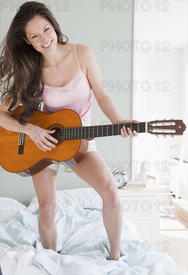 Mixed race woman playing guitar on bed