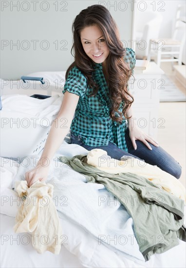 Mixed race woman sitting on bed with clothes