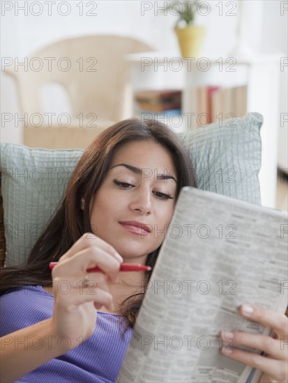 Hispanic woman doing newspaper crossword puzzle