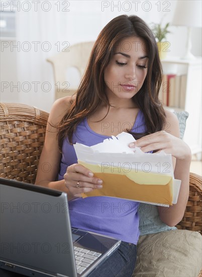 Hispanic woman holding laptop and looking through bills