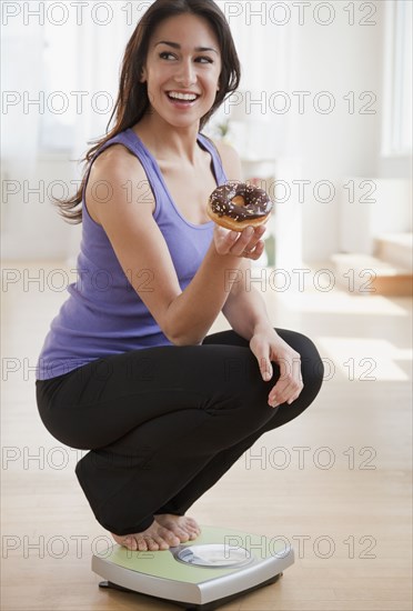 Hispanic woman holding donut and crouching on scale