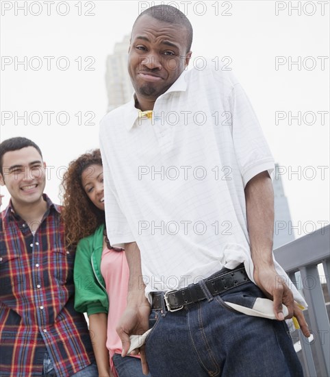 African man showing empty pockets with friends in background