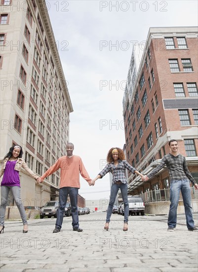 Friends holding hands and standing in a row on urban street