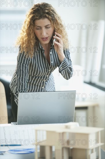 Hispanic architect using laptop and talking on cell phone