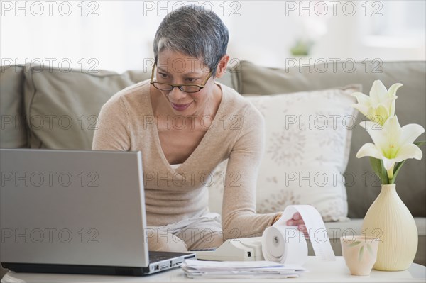 Chinese woman paying bills with laptop in living room