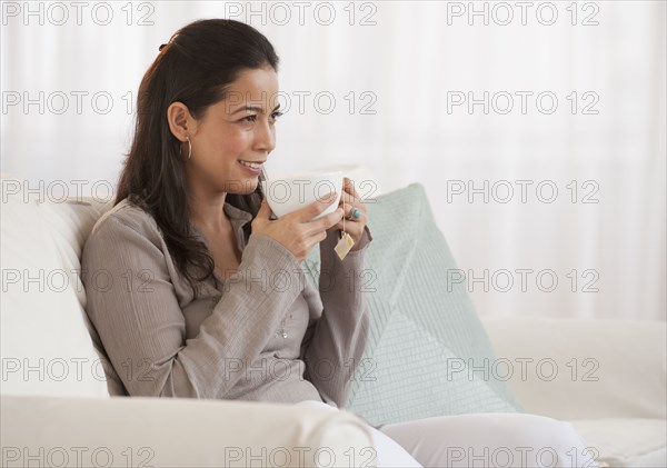 Hispanic woman drinking tea on sofa