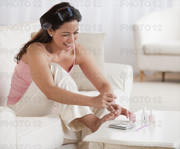 Hispanic woman painting toenails on sofa