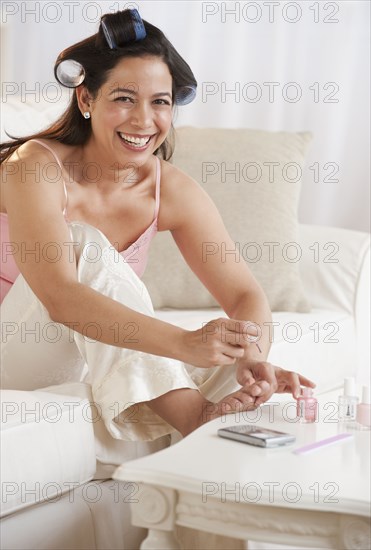 Hispanic woman painting toenails on sofa