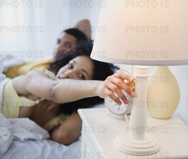 Woman in bed reaching to turn off bedside lamp