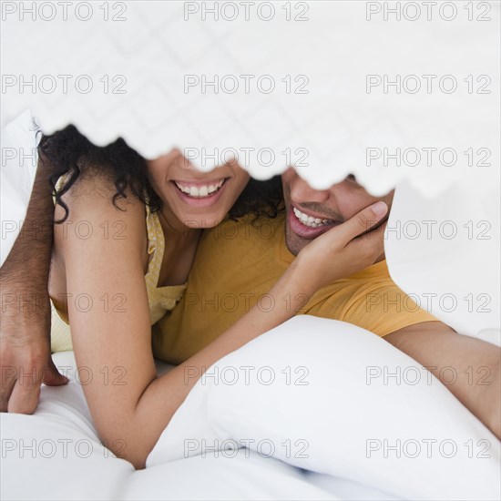 Smiling couple hiding under bed sheet