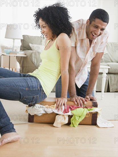 Couple stuffing clothes in small suitcase