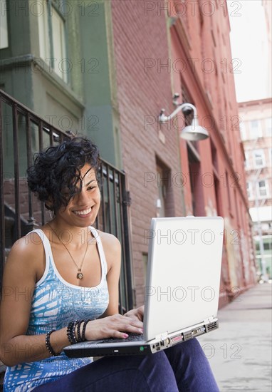 Mixed race woman using laptop on urban sidewalk