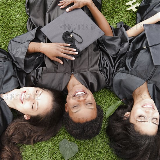 Friends in caps and gowns laying in grass