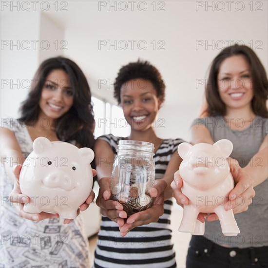 Friends holding out glass jar and piggy banks