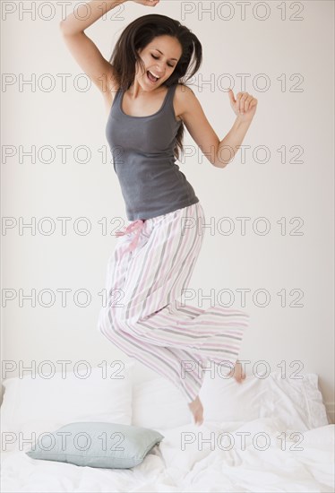 Mixed race woman jumping on bed