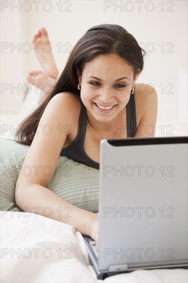 Mixed race woman typing on laptop in bed