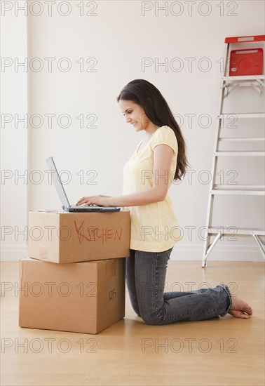 Mixed race woman using laptop on cardboard boxes